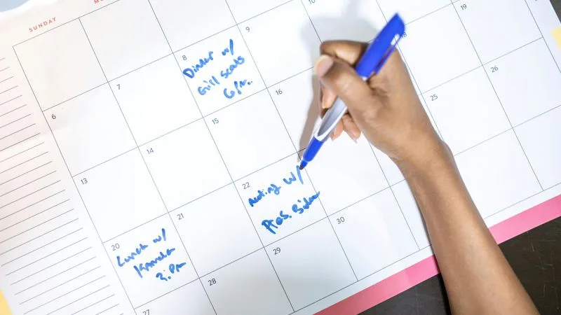 Person writing meeting minutes on a laptop with a calendar and notebook